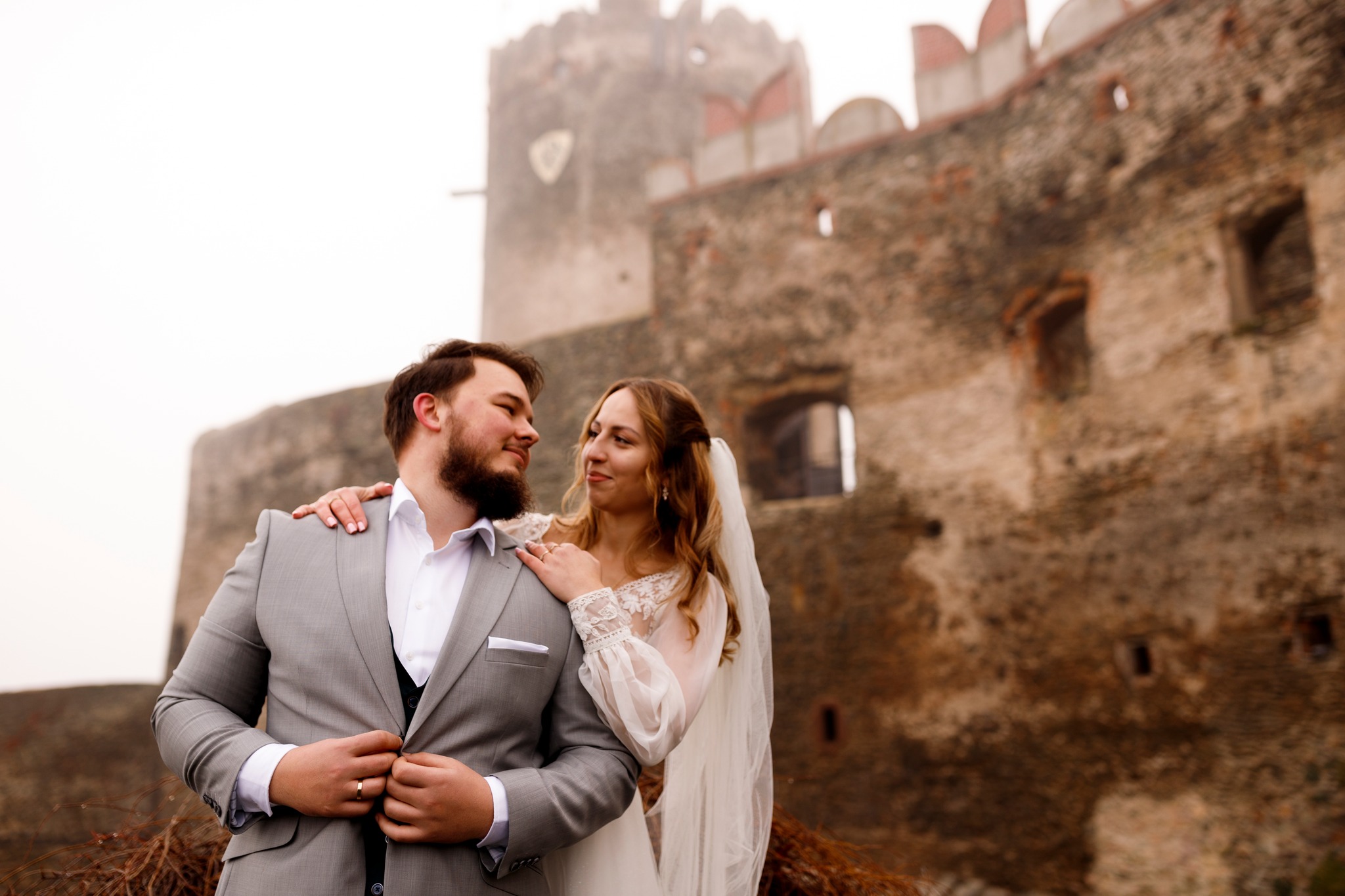 Romantyczna chwila podczas sesji ślubnej – para młoda na tle zamku we mgle